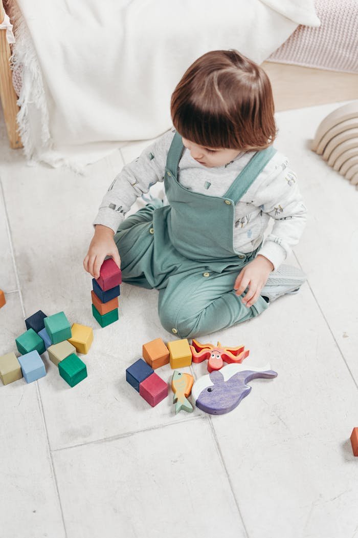 A young child sitting indoors, playing with colorful wooden blocks and toys, focused on building.