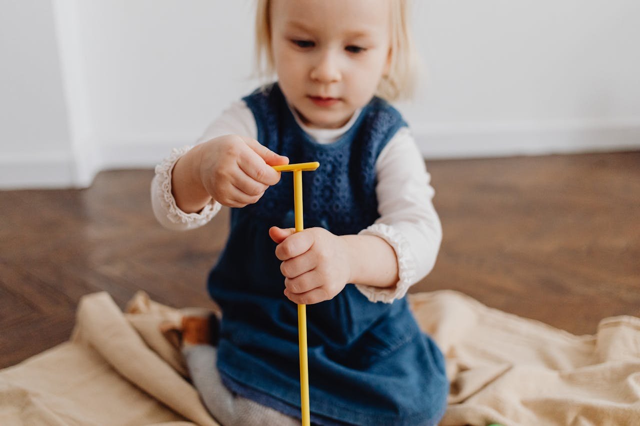 A young child playing indoors with a yellow stick, fostering creativity and imagination.