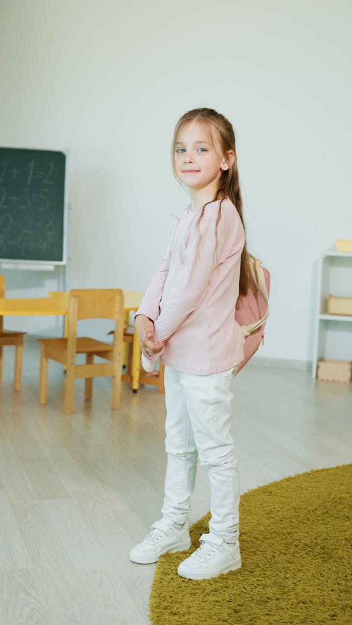 Cute young girl wearing a backpack, smiling in a classroom. Ideal for back-to-school themes.
