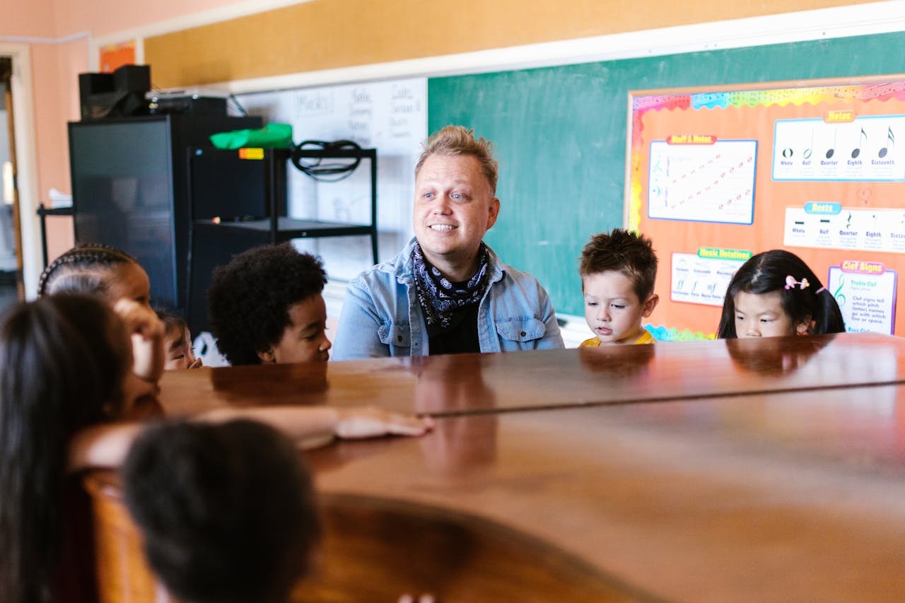 A teacher instructing young children in a music classroom, focused on piano learning.