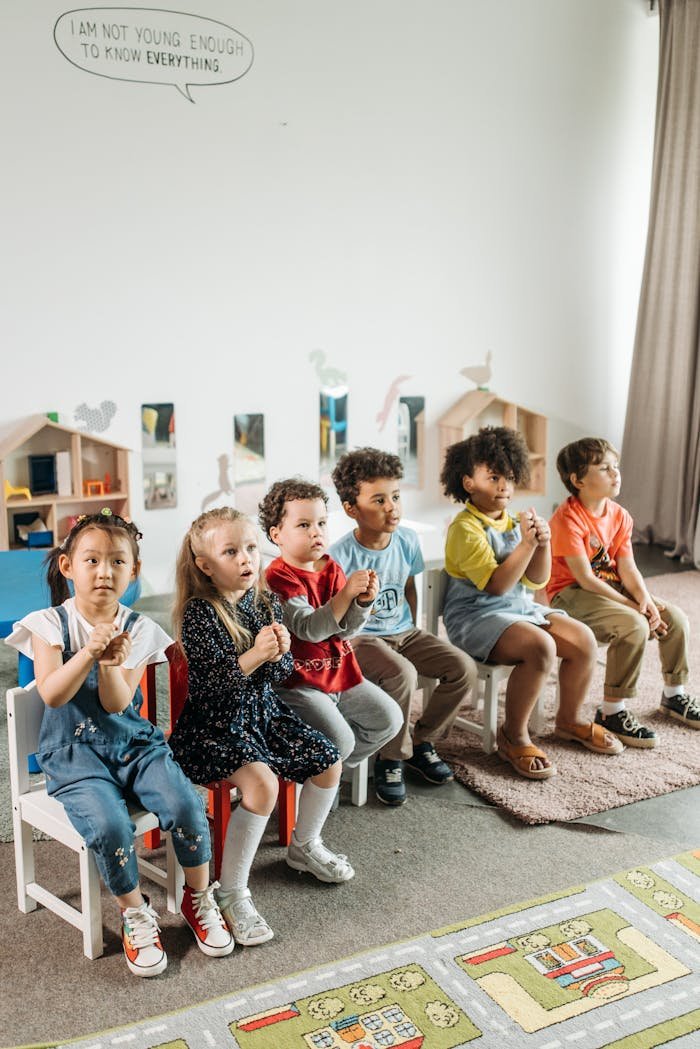 Children sitting together in a bright kindergarten classroom with toys and playful decor.
