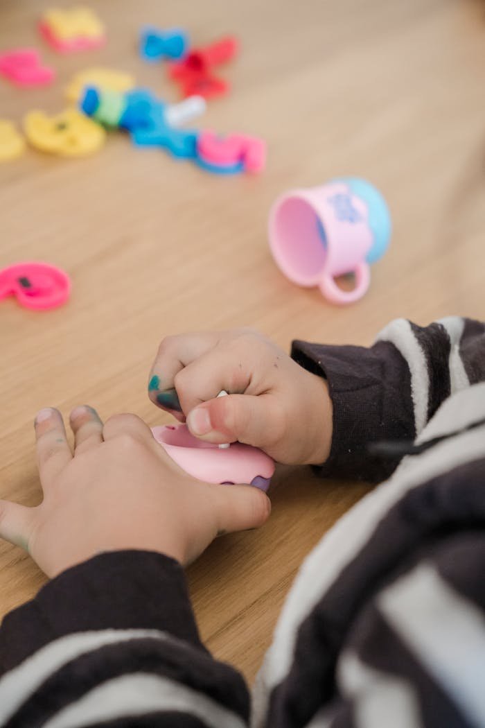 Close-up of a child playing with colorful plastic toys on a wooden surface indoors.