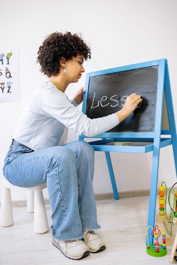 A preschool teacher writing on a blackboard in a classroom setting with educational toys.